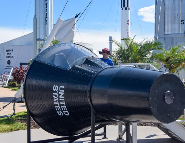 In the rocket garden at the Kennedy Space Center. Here Kenny is examining the insides of a Gemini two-seat spacecraft mockup prior to entering it. 